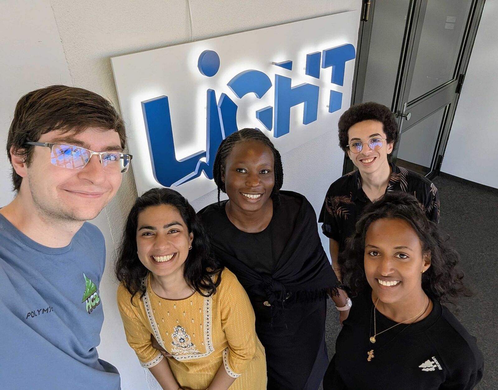 Omar and four lab mates smiling under the lit LiGHT sign