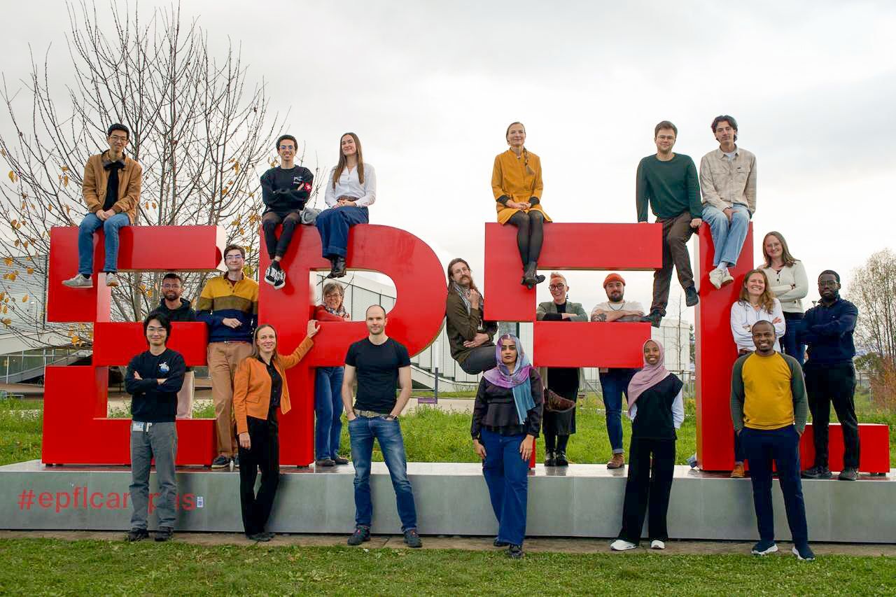 The LiGHT team sitting on and standing around the red EPFL letters