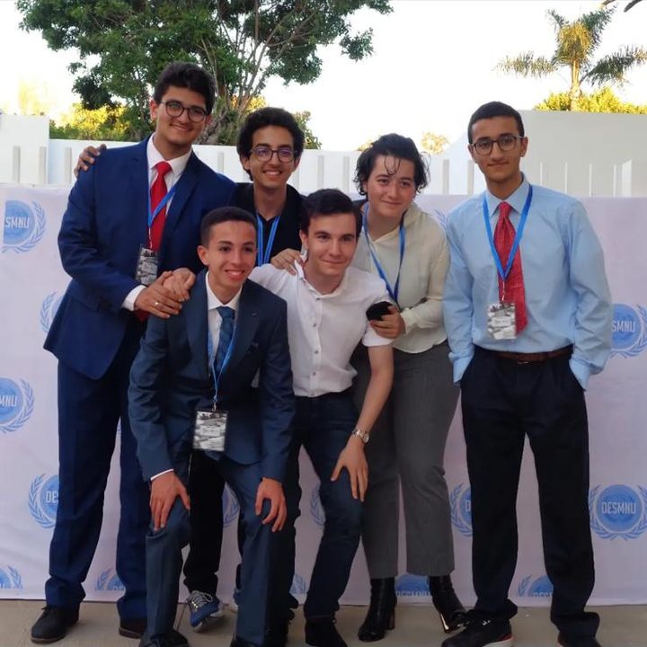 Seven delegates posing in front of a backdrop of DESMNU logos.