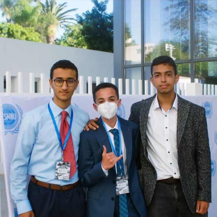 Three delegates posing in front of a DESMNU backdrop, one making a hand sign.