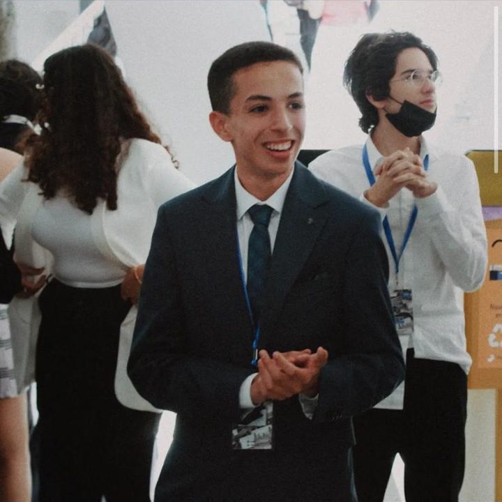A smiling delegate in a dark suit applauding among other delegates.