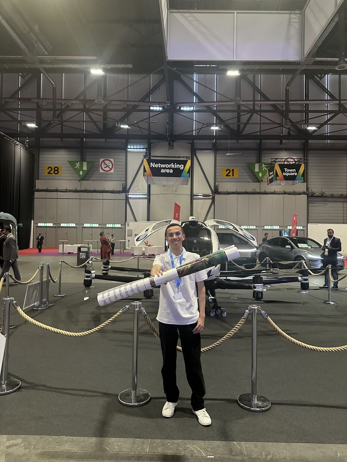 Omar holding a rolled poster in front of a passenger drone at the summit