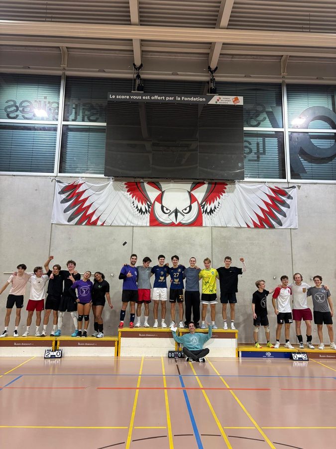 About twenty players lined up on the podium steps of a sports hall, under a banner of a red and white owl.