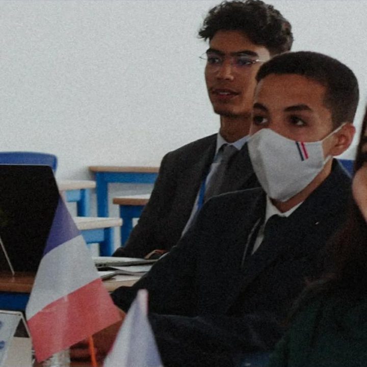 Masked delegates in suits at their desks, a French flag in front.