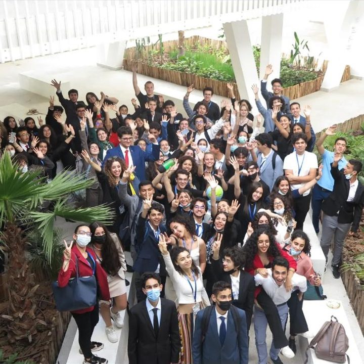 A large crowd of delegates waving from a staircase in a courtyard.